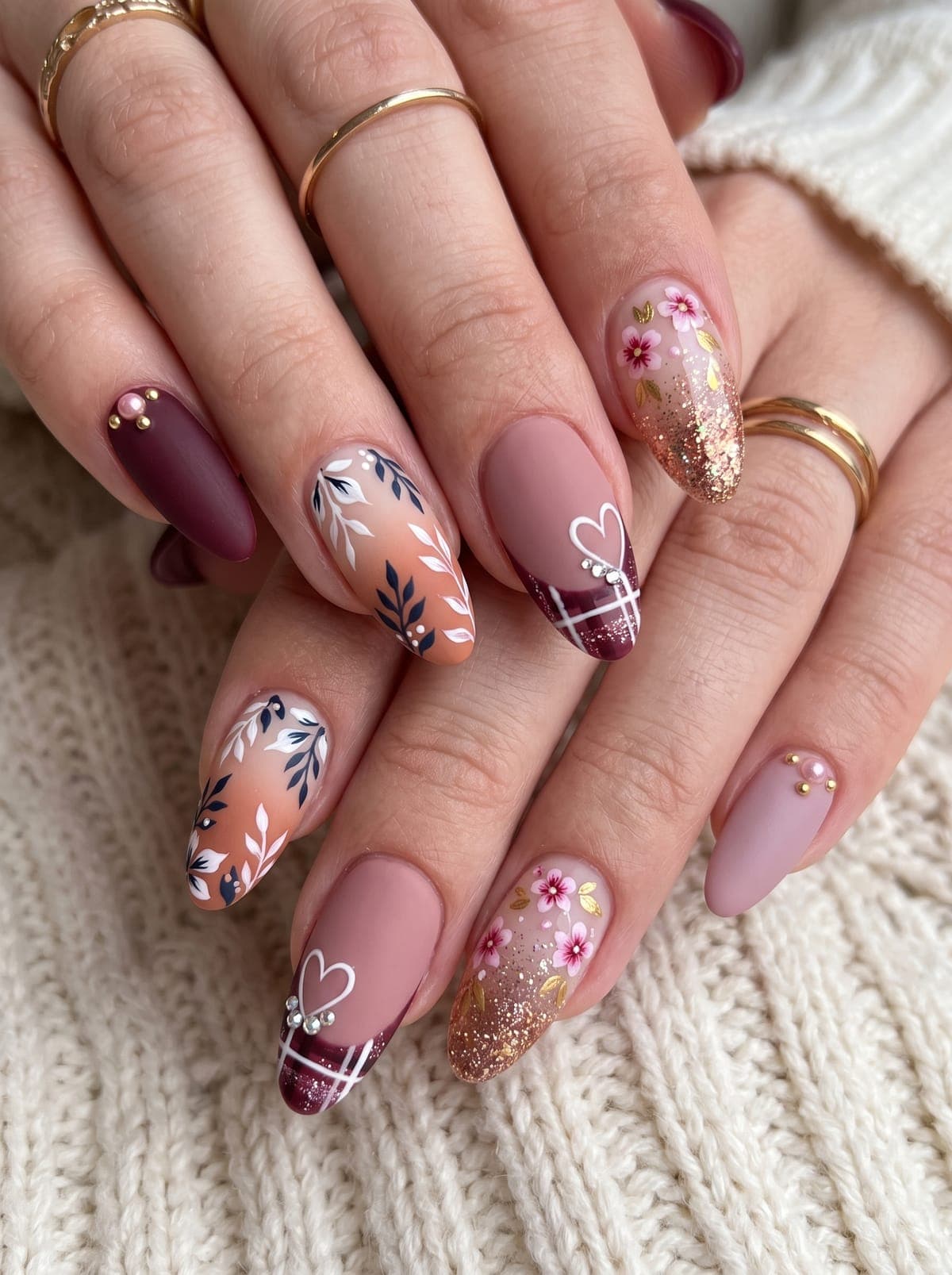 Almond nails in mauve, burgundy and peach with hand-painted leaves, flowers, plaid hearts and gold glitter