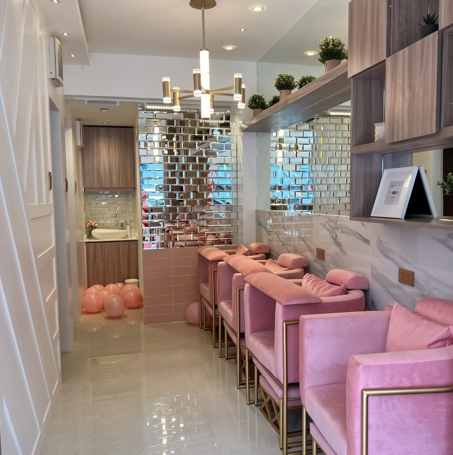 Pink velvet pedicure chairs with gold frames under a gold chandelier at Blush