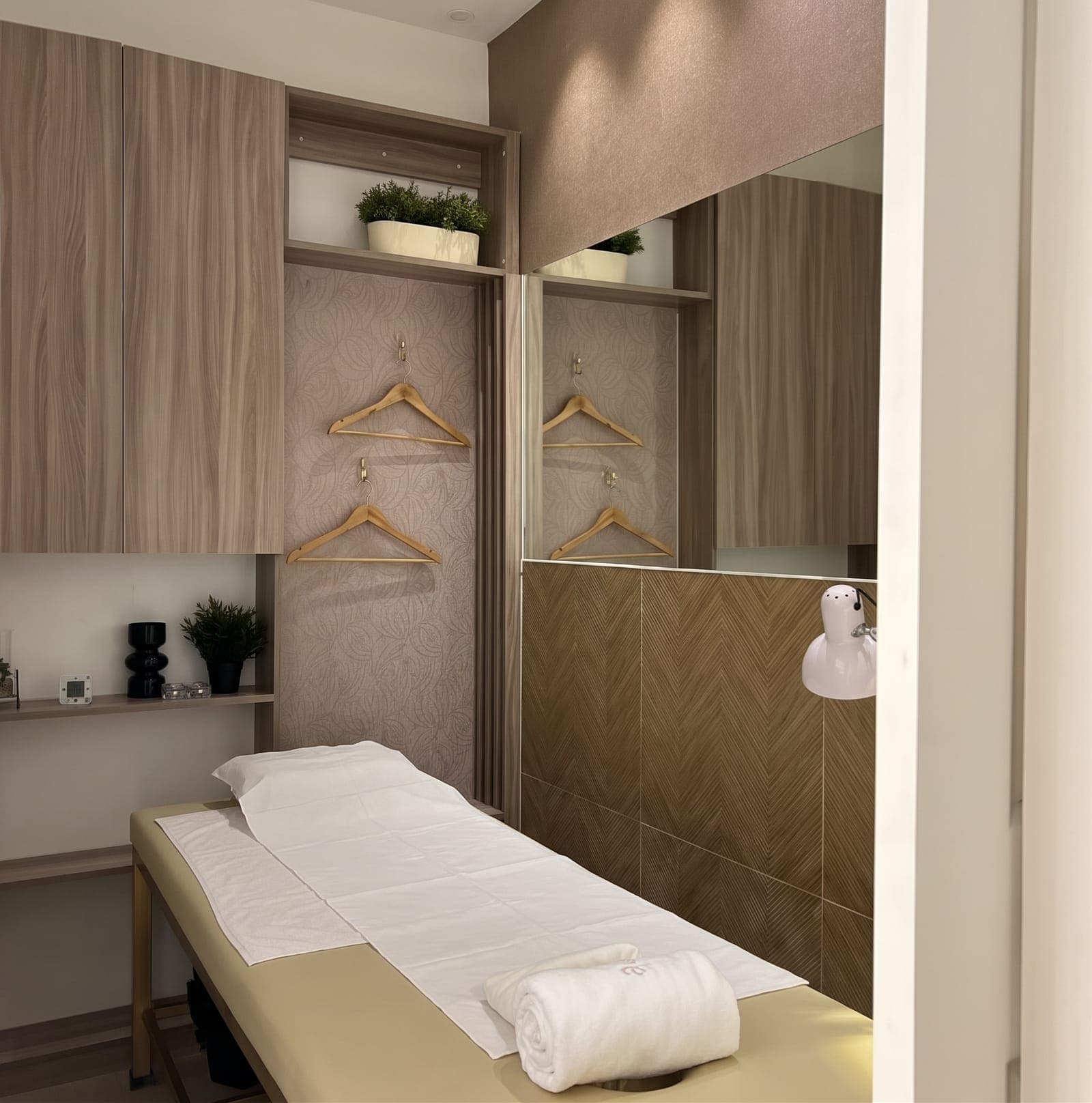 A calm treatment room with a made-up massage bed and a rolled towel
